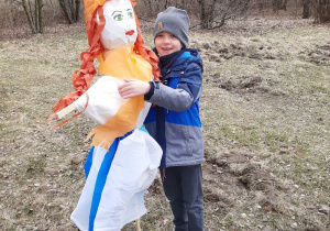 Uczeń klasy pierwszej trzyma Marzannę i pozuje z nią do zdjęcia.