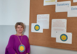 Pani wicedyrektor odznaczona Szkolnym Orderem Umiechu pozująca do zdjęcia na tle gazetki sciennej.