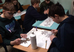 Uczniowie klasy 7 podczas pracy siedzący przy ławkach i malujący śnieżynki.
