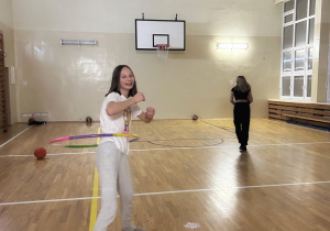 Dwie uczennice klasy ósmej w sali gimnastycznej. Jedna z nich kręci hula-hoop.