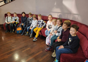 Klasa 1b siedząca na czerwonej kanapie w holu teatru.