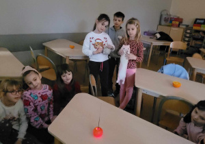 Dzieci skupione wokół stolika, na którym leży świecąca (za sprawą zimnych ogni) mandarynka imitująca słońce.