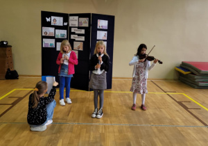 Dziewczynki podczas muzycznego występu. Jedna gra na skrzypcach, druga na flażolecie a trzecia śpiewa.