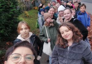 Uczniowie klasy piątej i nauczyciele na przystanku autobusowym.