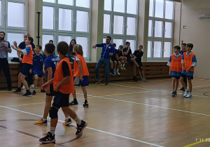 Chłopcy dwuch drużyn w sali gimnastycznej podczas rozgrywek koszykówki.