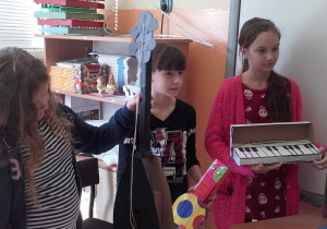 Trzy dziewczynki trzymają w rękach wykonane przez siebie instrumenty.