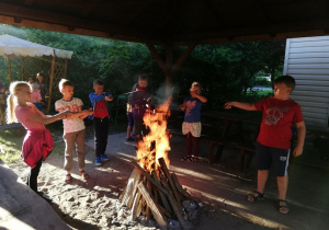 Dzieci zgromadzone wokół ogniska, piekące kiełbaski.
