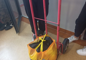 Na zdjęciu ręczny wózek magazynowy, na którym stoi torba z artykułami szkolnymi.