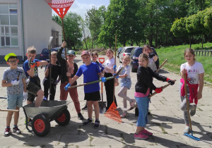 Na zdjęciu grupa uczniów klasy trzeciej gotowi do działań ogrodowych. Mają w rękach narzędzia i przyrządy ogrodnicze.