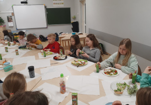 Dzieci z klasy drugiej siedzące przy stole i jedzące świąteczne śniadanie.
