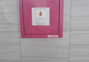 Na zdjęciu różowa skrzyneczka zawieszona na ścianie w damskiej toalecie.