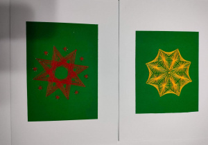 Leżące na ławce dwie kartki z wyszytymi gwiazdkami na zielonym tle papieru.