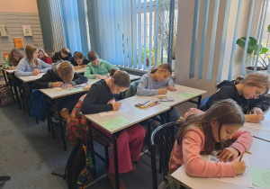 Uczniowie siedzący przy stolikach pochyleni nad zadaniem.