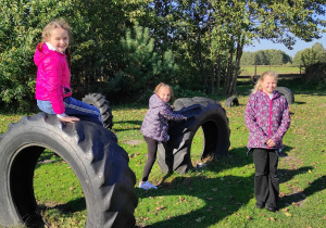 Trzy dziewczynki na torze przeszkód, wdrapujące się na wkopane opony od traktora.