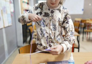 Uczennica klasy drugiej nawijająca na kartonik fioletową włóczkę.
