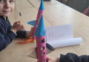 Dwoje uczniów prezentujących swoje różowo-niebieskie, tekturowe rakiety.