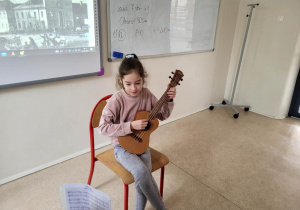 Dziewczynka siedząca na krzesełku i grająca na ukulele.