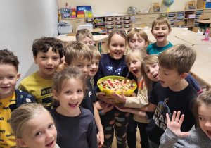 Na zdjęciu dzieci z klasy 1b prezentujący dużą miskę z samodzielnie wykonaną sałatką owocową.