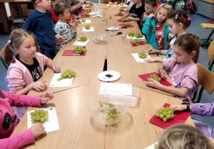 Dzieci siedzące przy stole z własnoręcznie wykonanymi jeżami na deseczkach.