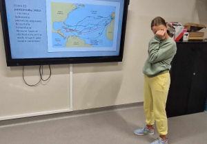Dziewczynka z klasy siódmej przy tablicy multimedialnej, pokazująca slajd swojej prezentacji.