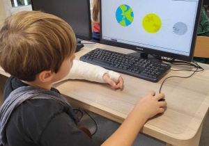 Chłopiec siedzący przed komputerem i rysujący w edytorze grafiki różne planety.