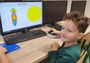 Chłopiec przed ekranem komputera na którym widać narysowaną rakietę i Słońce w edytorze grafiki Paint.