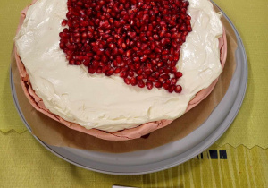 Ciasto z białym wierzchem na którym widnieje ułożona z nasion owocu granatu czerwona mapa Polski.