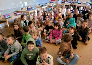 Dzieci z klasy pierwszej a i drugiej a, siedzące na podłodze podczas spotkania z pisarką Anną Kucharek.
