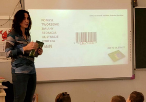 Autorka książek dla dzieci prezentująca jeden ze slajdów, zapoznaje dzieci z etapami powstawania książki.