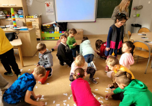 Dzieci szukające pasujących działań wśród rozrzuconych w sali karteczek.