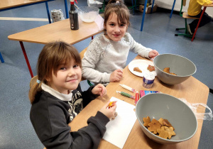 Dwie dziewczynki dekorujące pierniczki leżące przed nimi na talerzach.