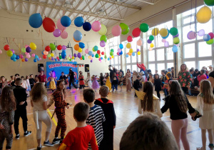 Dzieci w kole podczas tańca, w tle kolorowe dekoracje z balonów i serpentyn.