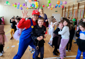 Wychowawczyni klasy 3b przebrana za Super Mario z jednym z uczniów. w tle pozostałe dzieci w tanecznej zabawie.