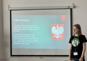 Uczennica na tle tablicy interaktywnej prezentuje informacje o Polsce i Łodzi.