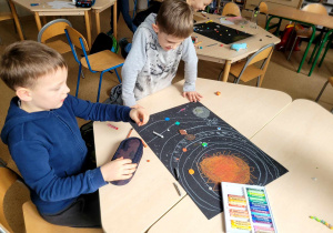 Dwaj chłopcy z pierwszej klasy przed nimi praca ich grupy przedstawiająca kosmos.