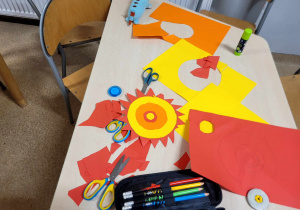 Słońce - praca wykonana z kolorowego papieru. Obok leżące na stoliku materiały i narzędzia wykorzystane w tej pracy.
