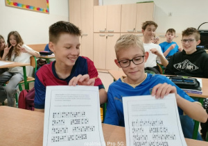 Dwóch uczniów z kartami związanymi z Dnie Kropki, za nimi ich koledzy i koleżanki.