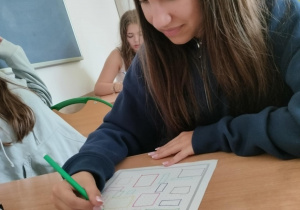 Uczennica pochylona nad kartką, rozwiązuje zadania matematyczne z kropkami w roli głównej.