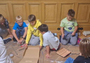 Grupa chłopców podczas pracy, przednimi filia, tektura, platonki po jajkach i inne przybory.