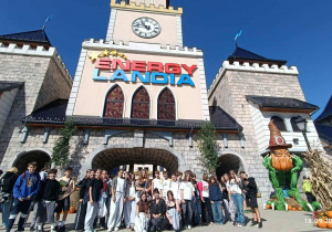 Uczniowie klasy siódmej i ósmej pozujący do wspólnego zdjęcia na tle zamku z napisem Energylandia, czyli przed wejściem do parku rozrywki.