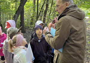 Dzieci uważnie słuchające prowadzącego warsztaty, prezentującego gałązkę jednego z drzew.