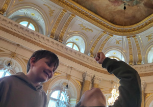 Dwóje dzieci w zamkowych wnętrzach patrzące w górę, podziwiające malowidła na suficie.