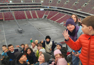 Dzieci z klasy 3b na trybunach, w tle tafla boiska i trybuny.