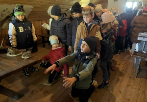 Dzieci stojące jedno za drugim, dwoje z nich klęczy na woreczku z grochem, aby sprawdzić jakie dawniej stosowano kary w szkołach.