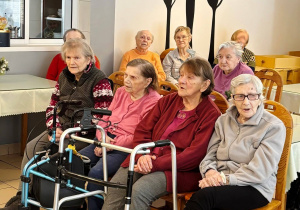 Grupa pensjonariuszy Domu Pomocy Społecznej siedząca na widowni śpiewająca wraz z dziećmi kolędy.