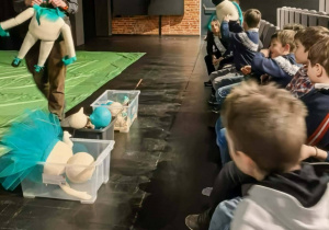 Dzieci siedzące na widowni, przed nimi prowadzący warsztaty prezentujący lalki.