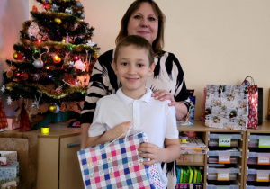 Chłopiec z klasy 3a z prezentem w ręku pozujący do zdjęcia z wychowawczynią, w tle klasowa choinka.