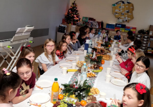 Uczniowie klasy 3a zasiadający przy nakrytym stole, świątecznie udekorowanym i zastawionym smakołykami.
