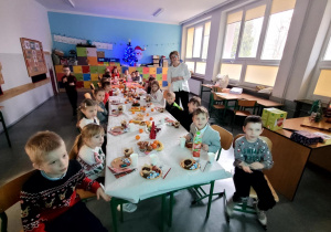 Dzieci przy nakrytym i zastawionym smakołykami stole.