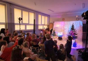 Aktorka zasłaniająca się walizką, przed piłeczkami-śnieżkami rzucanymi przez dzieci z widowni.